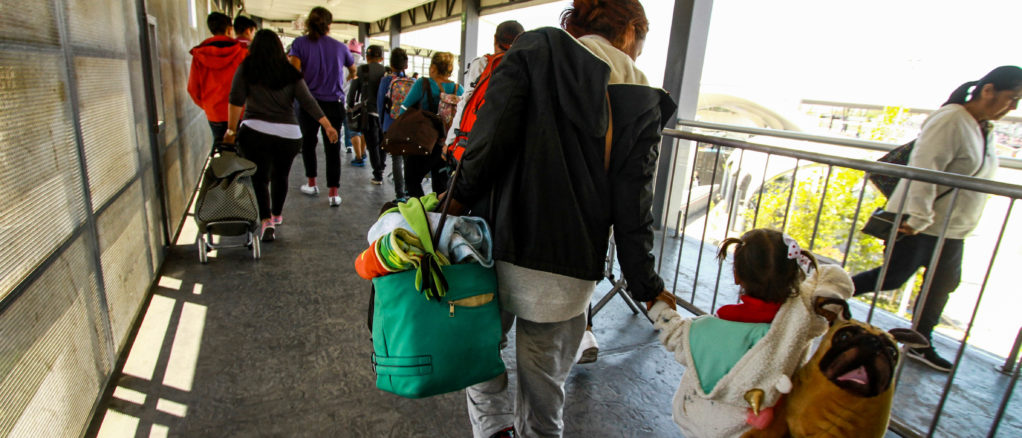 Madres y niños de la caravana migrante cruzan el puente peatonal