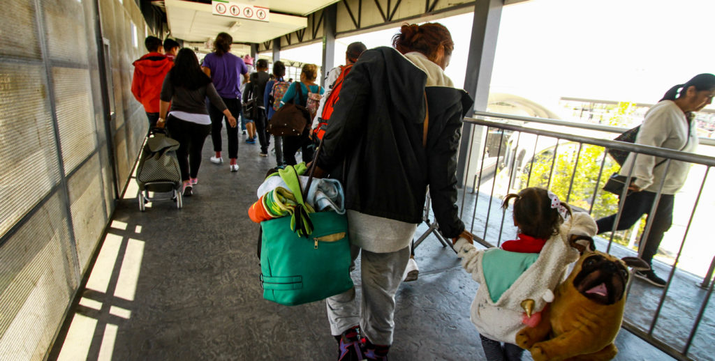 Madres y niños de la caravana migrante cruzan el puente peatonal